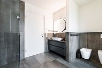 Modernes Badezimmer mit grauen Fliesen, weißem Waschbecken und runder beleuchteter Spiegel