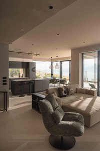 Modernes Wohnzimmer mit Küche, Sofa und Panoramafenstern mit Blick auf Landschaft und Meer