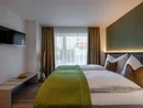 Modernes Hotelzimmer mit zwei Betten, grünem Tagesdecke und Wandfernseher