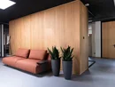 Modernes Büro mit braunem Sofa, Holzwand und zwei hohen Pflanzgefäßen