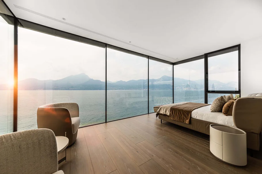 Modernes Schlafzimmer mit Panoramafenster und Blick auf See und Berge bei Sonnenuntergang