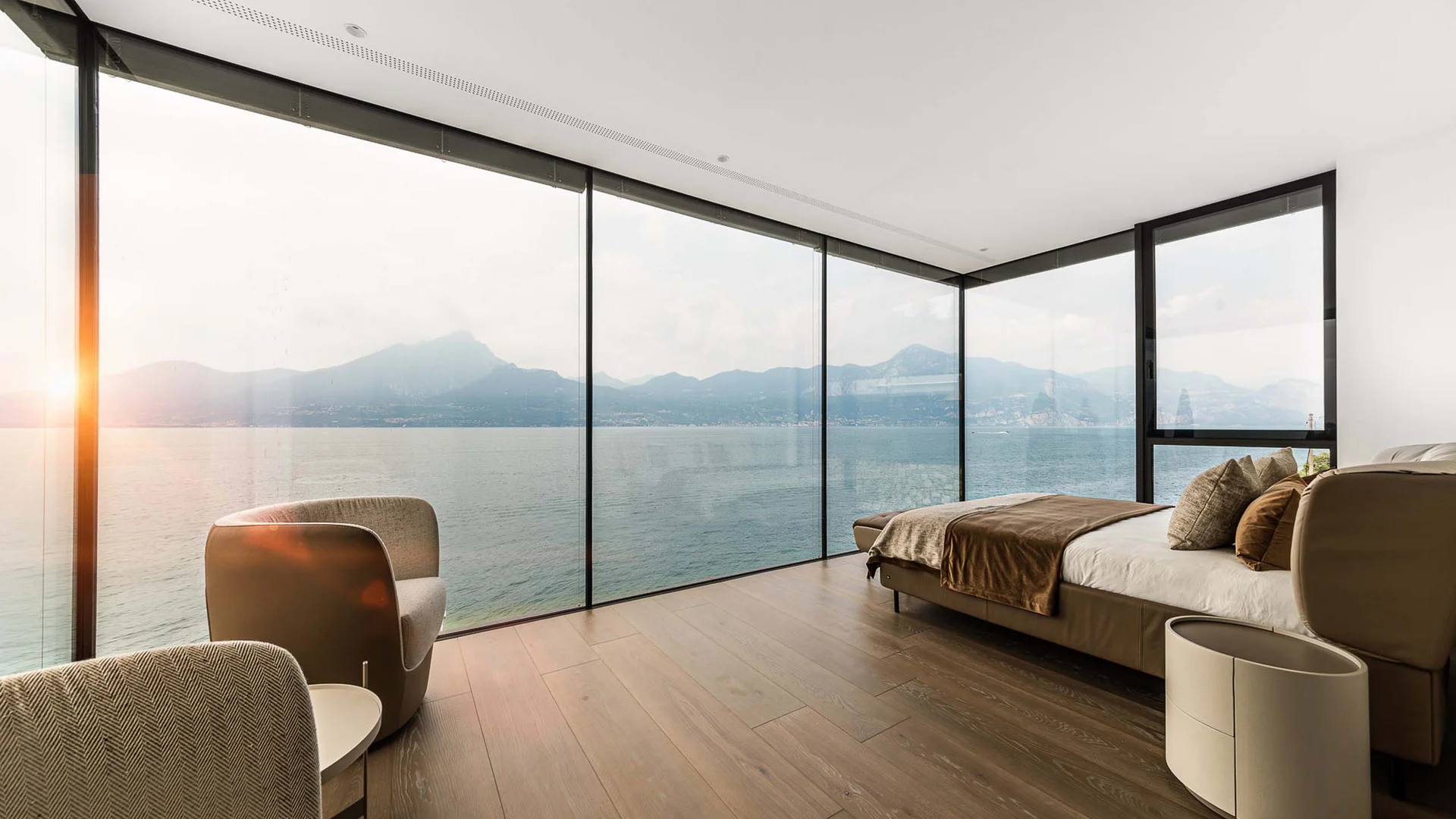 Modernes Schlafzimmer mit Panoramafenster und Blick auf See und Berge bei Sonnenuntergang