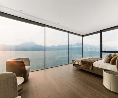 Camera da letto moderna con finestra panoramica e vista sul lago e sulle montagne al tramonto
