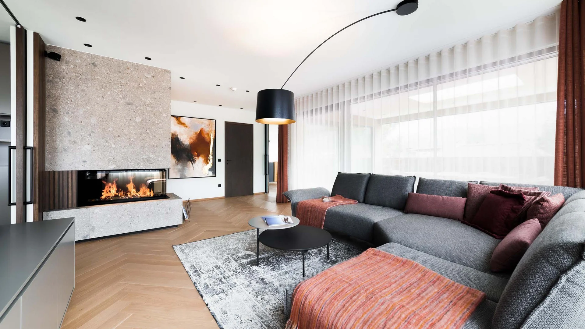 Moderner Wohnzimmer mit grauem Sofa, Kamin und großen Fenstern mit weißen Vorhängen