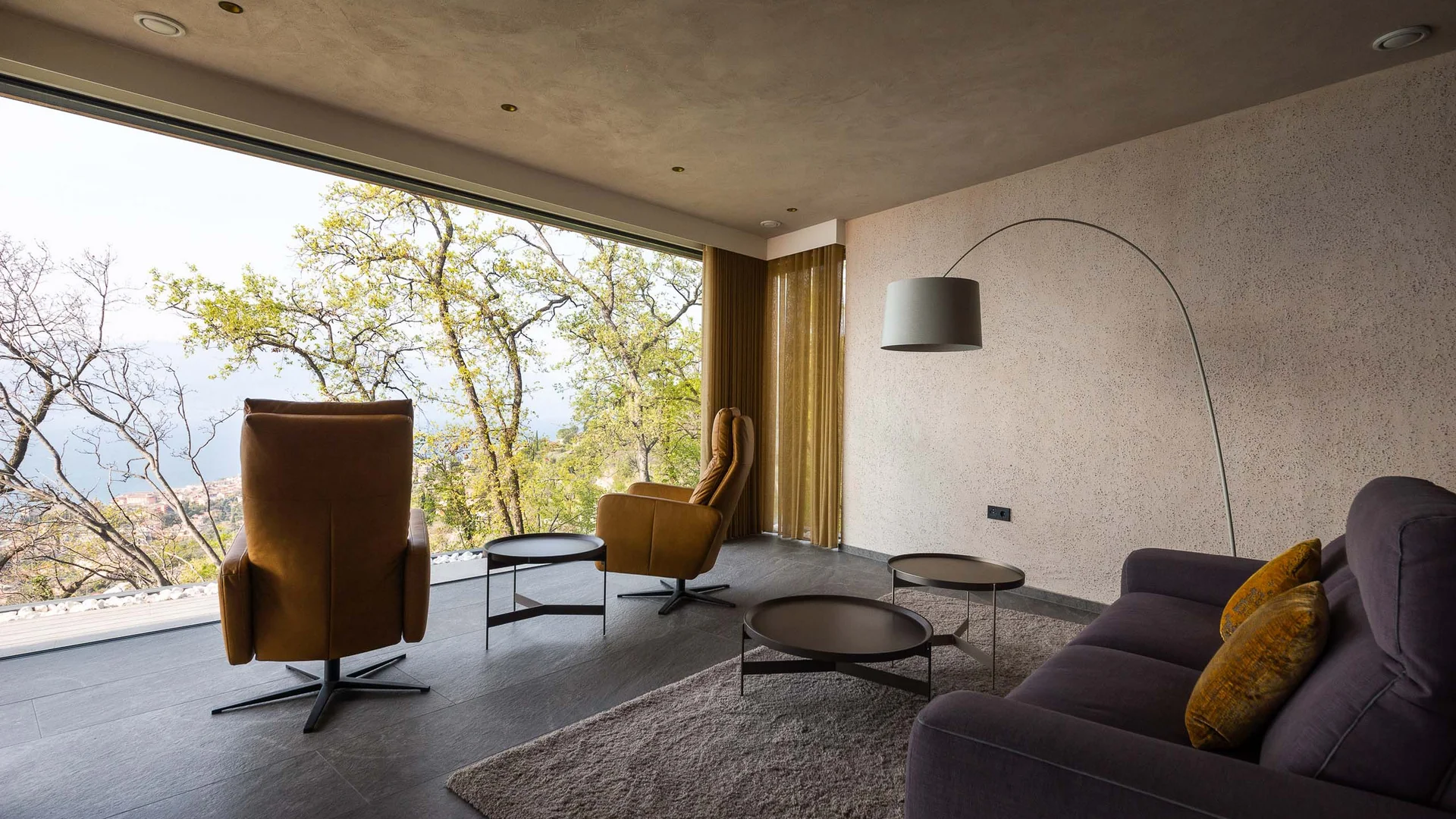 Modernes Wohnzimmer mit großen Fenstern und Blick auf Bäume und Landschaft