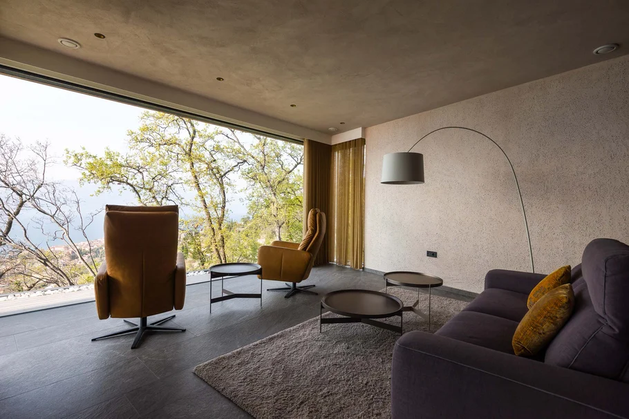 Modernes Wohnzimmer mit großen Fenstern und Blick auf Bäume und Landschaft
