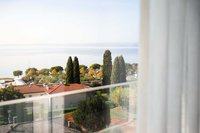 Blick auf See, Bäume und Häuser durch ein Fenster mit Vorhang