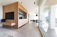 Moderner Wohnbereich mit Holzregalen, Fernseher und Essbereich neben großen Fenstern