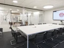 Moderner Konferenzraum mit großem Tisch, schwarzen Stühlen und Bildschirm an der Wand