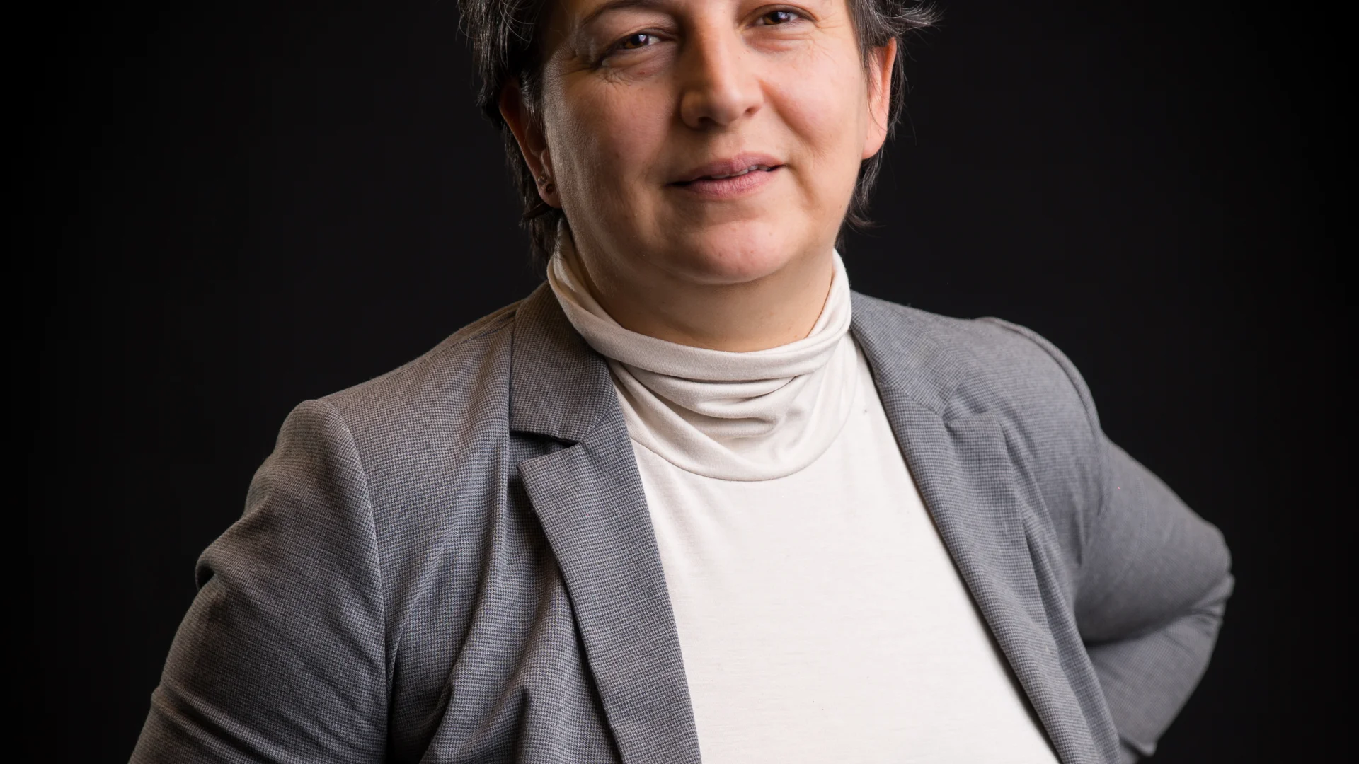 Portrait einer Person in grauem Blazer vor schwarzem Hintergrund