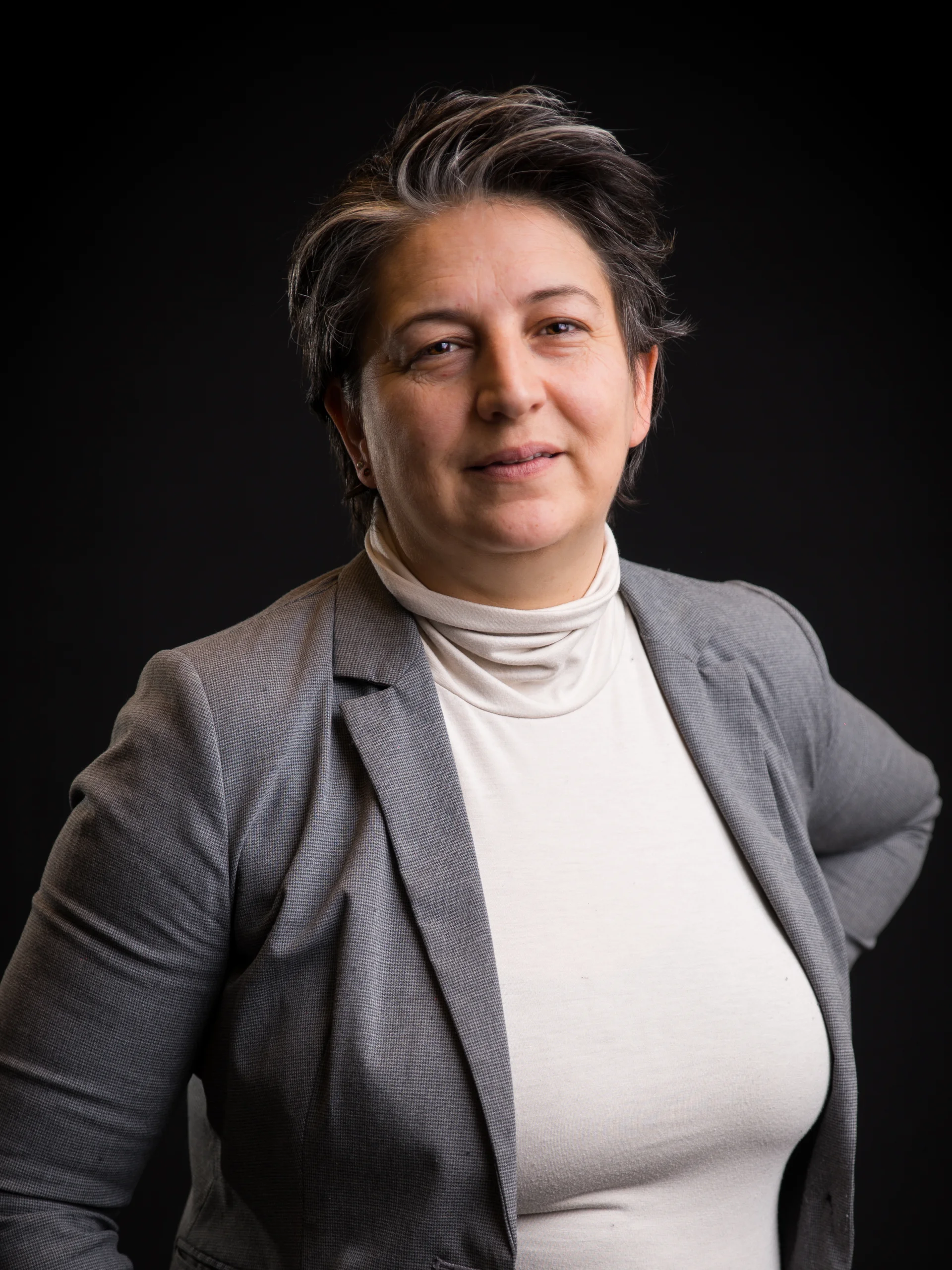 Portrait einer Person in grauem Blazer vor schwarzem Hintergrund