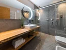Modernes Badezimmer mit Holzablage, beleuchtetem Spiegel und Glasdusche
