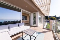 Moderner Balkon mit Sofa, Tisch und Glasbrüstung mit Blick auf grüne Landschaft