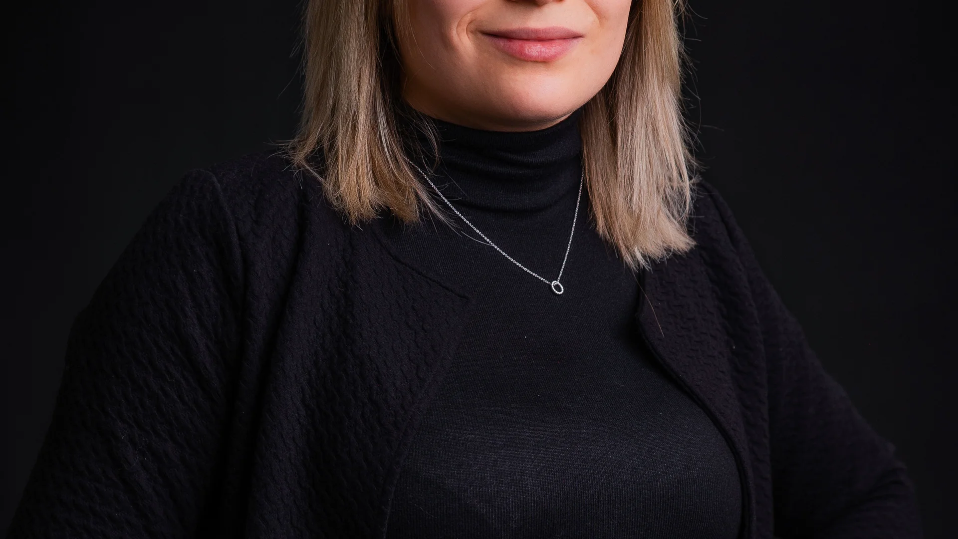 Porträt einer Frau mit Brille und schwarzem Pullover vor schwarzem Hintergrund