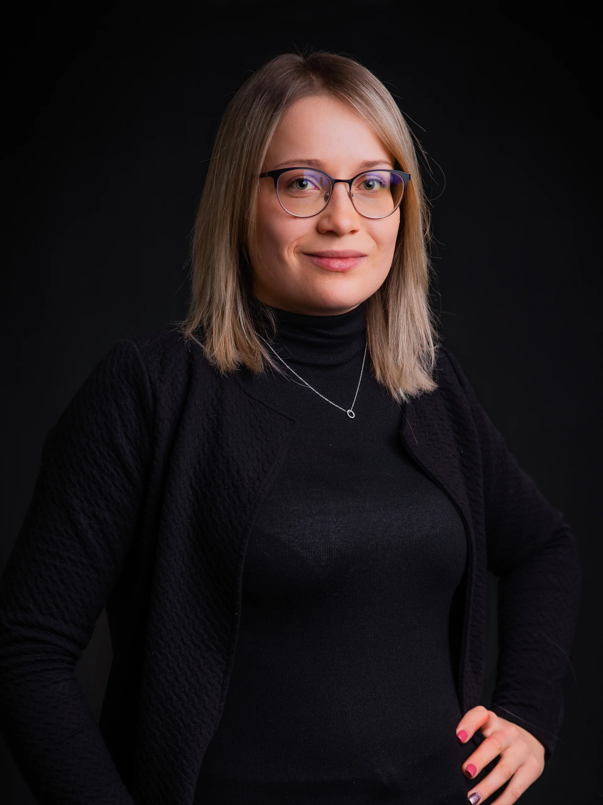 Porträt einer Frau mit Brille und schwarzem Pullover vor schwarzem Hintergrund