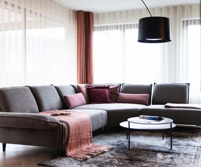 Helles Wohnzimmer mit grauem Ecksofa, rosa Kissen und Rundtisch