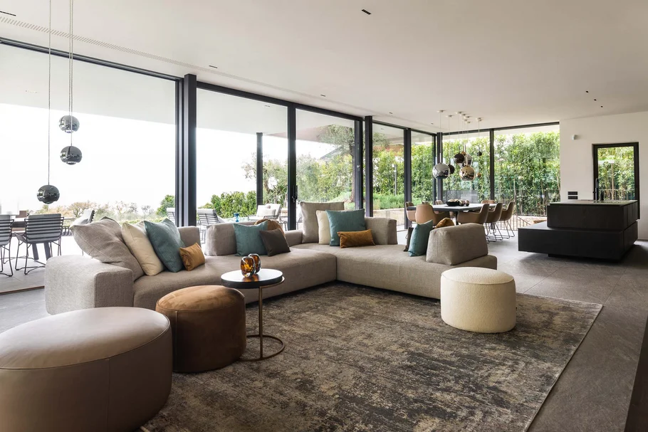 Moderner Wohnbereich mit Ecksofa, Sitzhockern und großen Glasfenstern