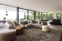 Moderner Wohnbereich mit Ecksofa, Sitzhockern und großen Glasfenstern