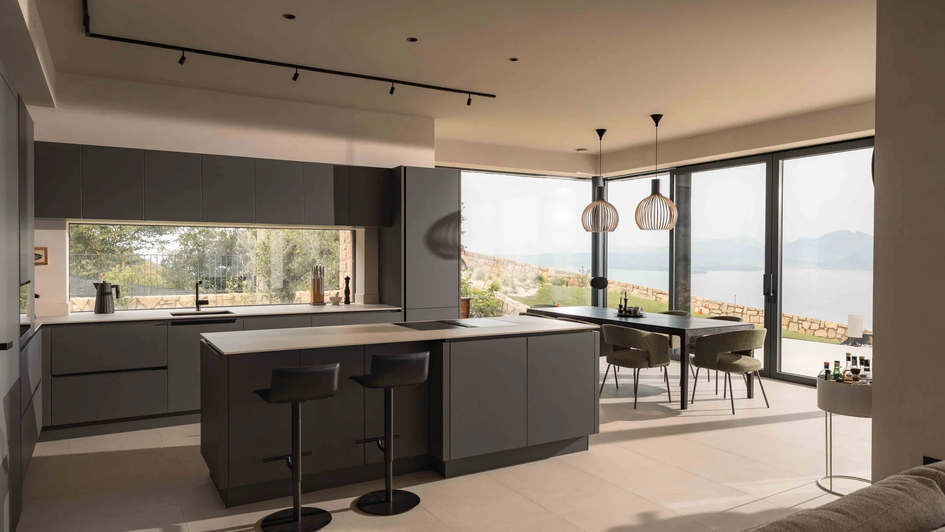 INTERIOS. Il tuo studio di interior design. Cucina moderna con isola, zona pranzo e vista sul lago dalle ampie finestre