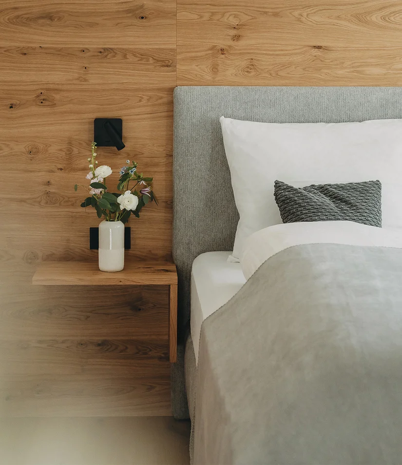 Letto matrimoniale con testiera grigia, parete in legno e vaso di fiori sul comodino
