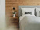 Letto matrimoniale con testiera grigia, parete in legno e vaso di fiori sul comodino
