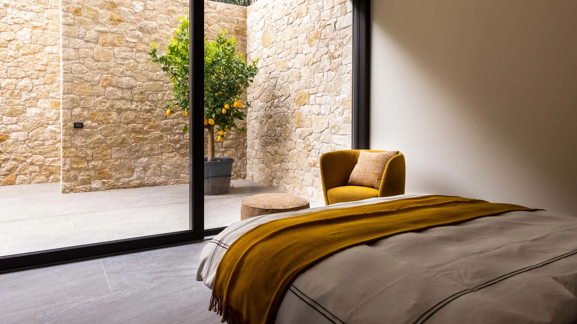 Schlafzimmer mit gelbem Sessel und Blick auf Zitronenbaum hinter Glaswand