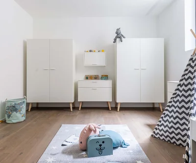 Camera dei bambini luminosa con armadi bianchi, tappeto da gioco e tenda