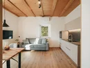 Soggiorno accogliente con divano grigio, soffitto con travi in legno e cucina integrata
