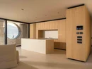INTERIOS. Il tuo studio di interior design. Soggiorno moderno con cucina in legno chiaro, isola e finestra circolare