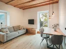 Soggiorno con divano grigio, tavolo in legno, sedie e soffitto con travi in legno