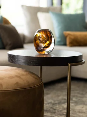 Moderner Wohnzimmertisch mit braunem Glasaccessoire und Sofa im Hintergrund