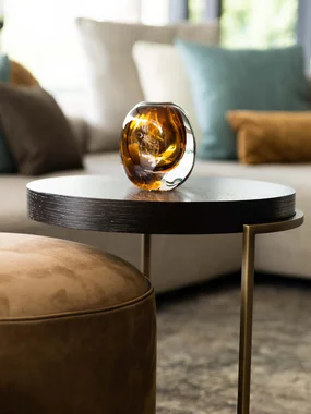 Tavolino moderno con decorazione in vetro marrone e divano sullo sfondo