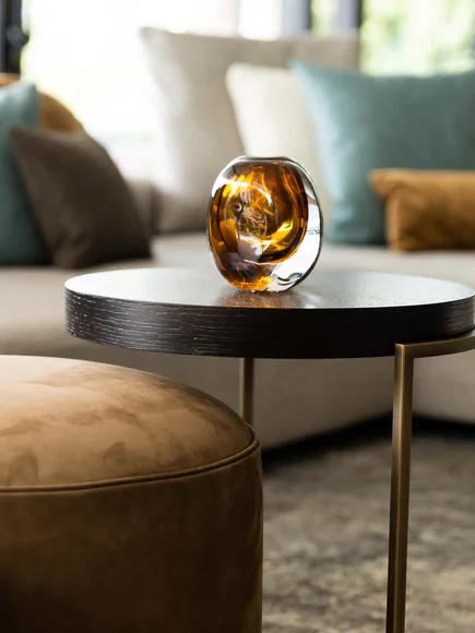 Moderner Wohnzimmertisch mit braunem Glasaccessoire und Sofa im Hintergrund