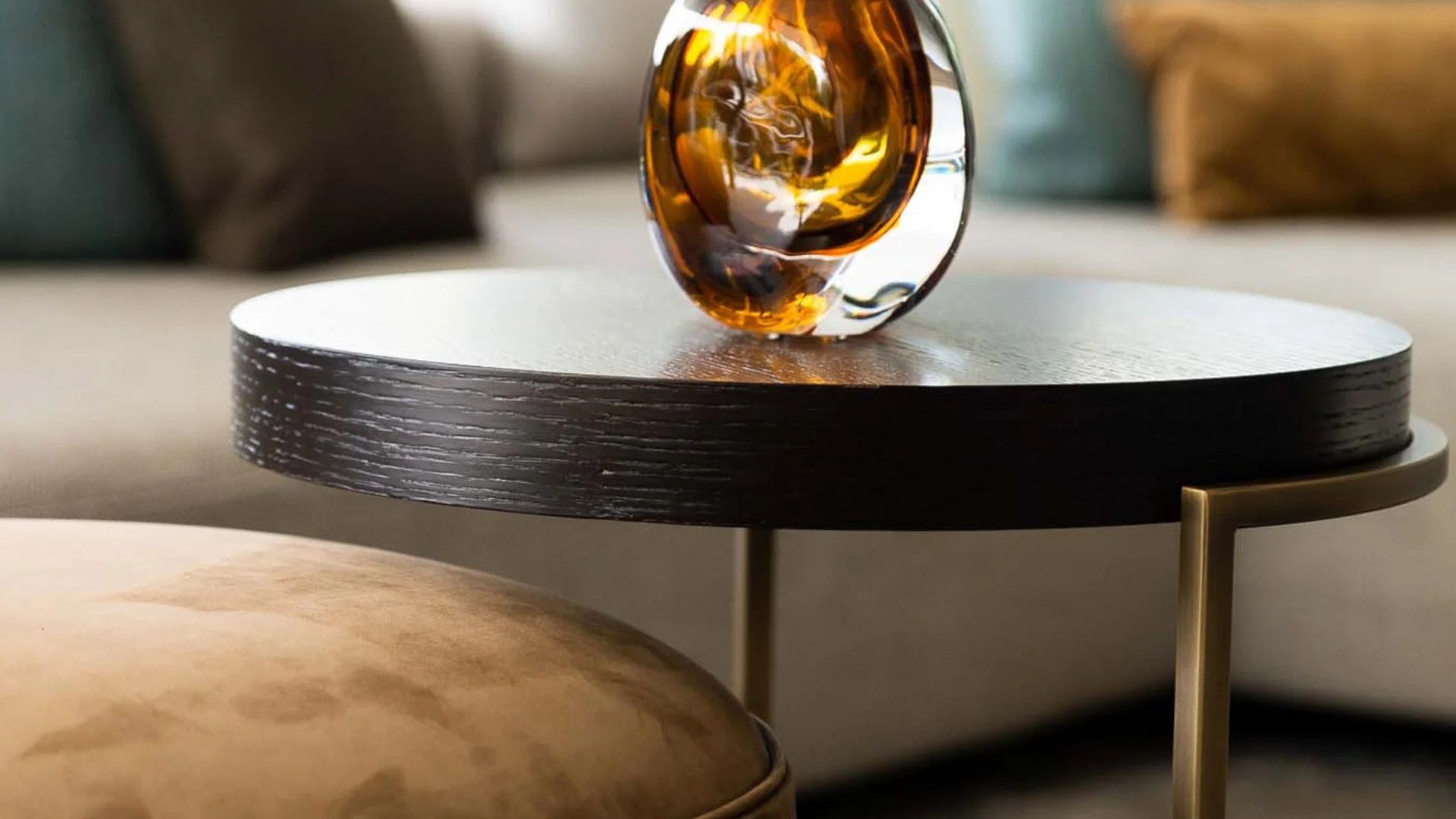 Moderner Wohnzimmertisch mit braunem Glasaccessoire und Sofa im Hintergrund
