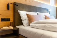 Modernes Hotelbett mit Kissen, Leselampe und Nachttisch mit Buch