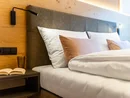 Modernes Hotelbett mit Kissen, Leselampe und Nachttisch mit Buch