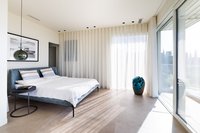 Helles modernes Schlafzimmer mit großem Fenster, blauem Bett und Vorhängen