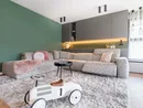 Modernes Wohnzimmer mit grauem Ecksofa, grünem Wandakzent und Kinderspielzeug-Auto