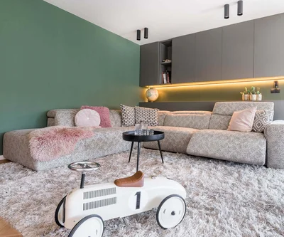 Modernes Wohnzimmer mit grauem Ecksofa, grünem Wandakzent und Kinderspielzeug-Auto