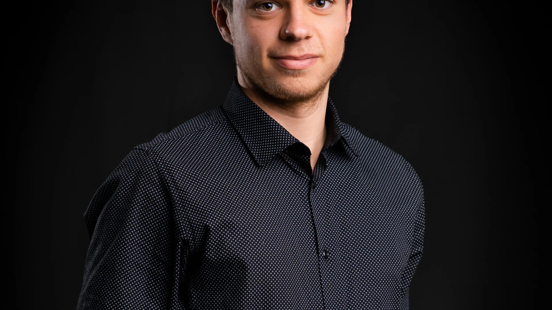 Junger Mann in dunkelblauem Hemd vor schwarzem Hintergrund