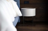 Moderner weißer Nachttisch neben einem blauen Bett vor dunkler Holzwand