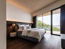 Modernes Schlafzimmer mit großem Bett und Balkon mit Blick auf grüne Hügel