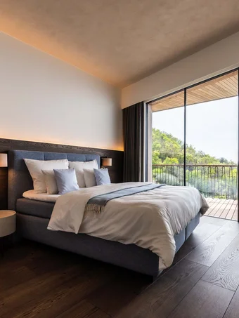 Modernes Schlafzimmer mit großem Bett und Balkon mit Blick auf grüne Hügel