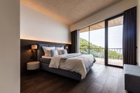 Modernes Schlafzimmer mit großem Bett und Balkon mit Blick auf grüne Hügel