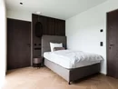 Modernes Schlafzimmer mit Einzelbett, dunklen Holztüren und hellem Parkettboden