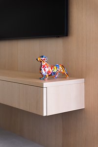 Bunte Dackel-Statue auf hellem Holzregal unter einem Fernseher