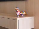 Bunte Dackel-Statue auf hellem Holzregal unter einem Fernseher