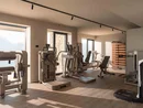 INTERIOS. Il tuo studio di interior design. Sala fitness luminosa con attrezzi e grandi finestre affacciate sulle montagne