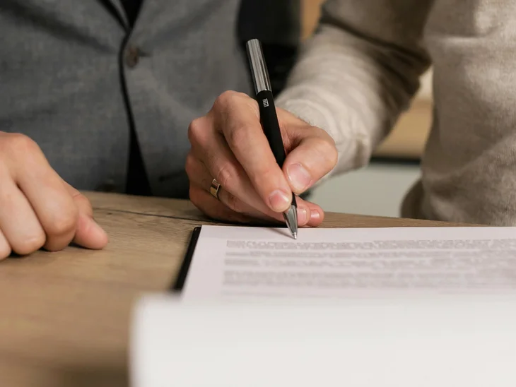 Persona che firma un documento mentre un'altra persona è accanto a lei