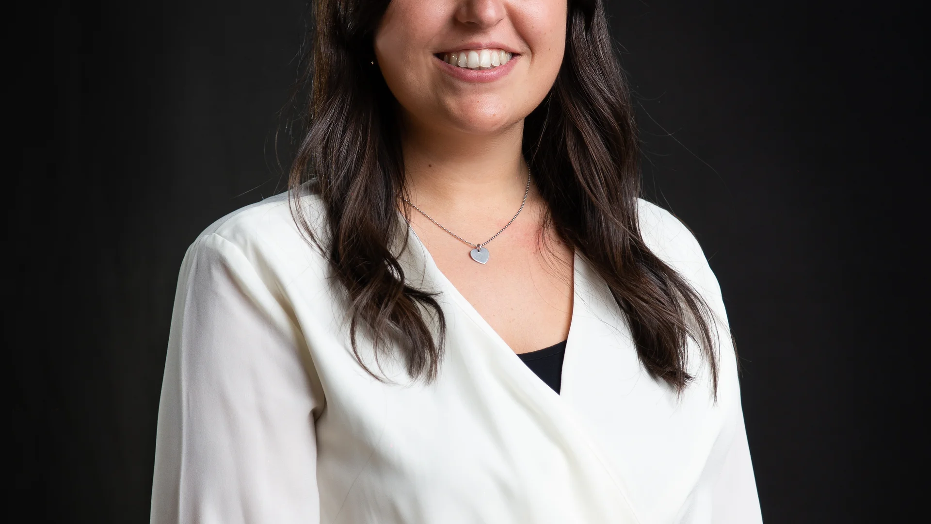 Porträt einer lächelnden Frau mit weißer Bluse vor schwarzem Hintergrund